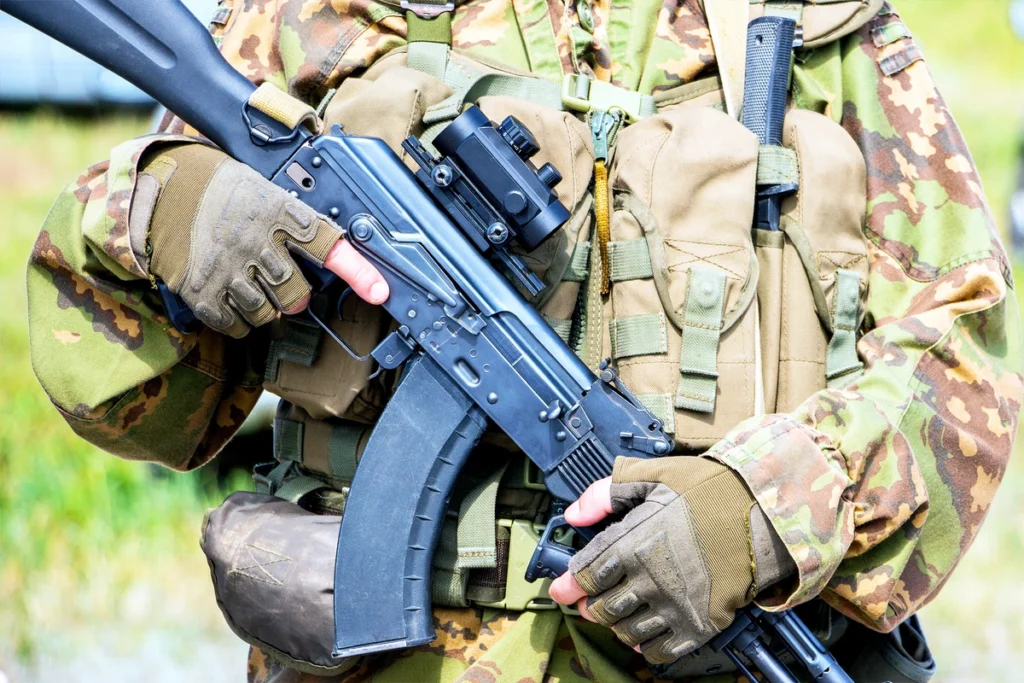 A soldier wearing tactical gloves holds a rifle