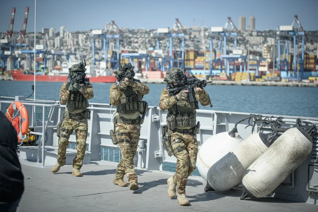 Three special forces operators in tactical MOLLE vests on a ship deck, armed with assault rifles.