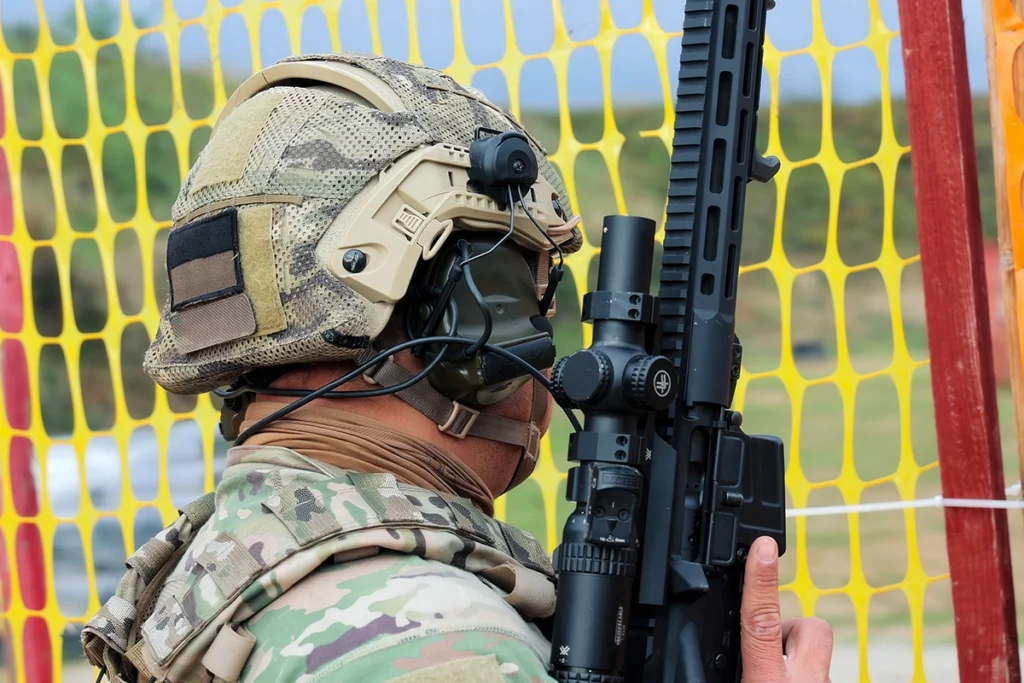 soldier in camouflage wearing a ballistic helmet and holding an assault rifle near a safety net