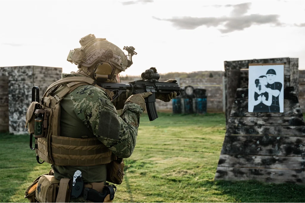 Żołnierz w kompletnej odzieży balistycznej, w tym kamizelce plate carrier i hełmie, celuje do tarczy na strzelnicy