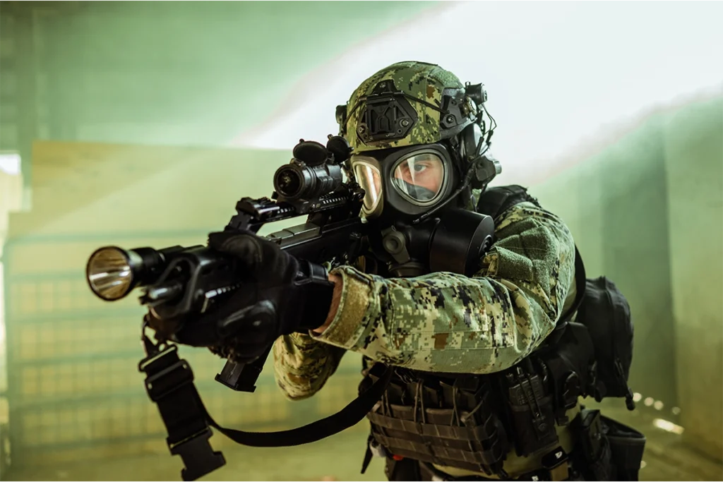 Operator sił specjalnych w masce przeciwgazowej i hełmie, stanowiących element kompletnej odzieży balistycznej, celuje z karabinu