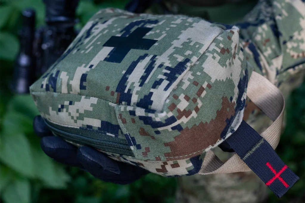 An operator in a tactical glove holding a closed camouflage IFAK pouch